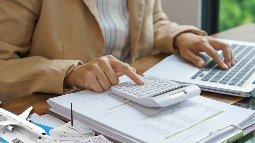 Person's hands shown working on calculator and laptop processing expenses.